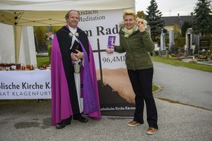 Stadträtin Sandra Wassermann und Stadtpfarrer Gerhard Simonitti verteilen Weihwasser am Eingang des Zentralfriedhofs. Foto: StadtKommunikation/Hude