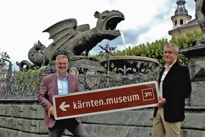 Adi Kulterer, Vorstand Tourismusverband Klagenfurt am Wörthersee, und Tourismusstadtrat Max Habenicht mit einem Beispielschild vorm Lindwurm. Foto: Büro Habenicht